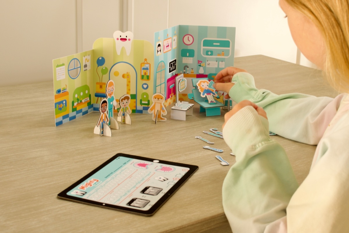 A child playing with the Mighty Pack — assembled dental office scene alongside the Mighty Pedia app on a tablet